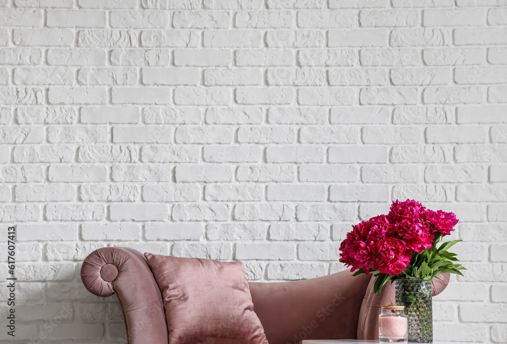 Vase of red peonies with candle on coffee table and couch near white brick wall