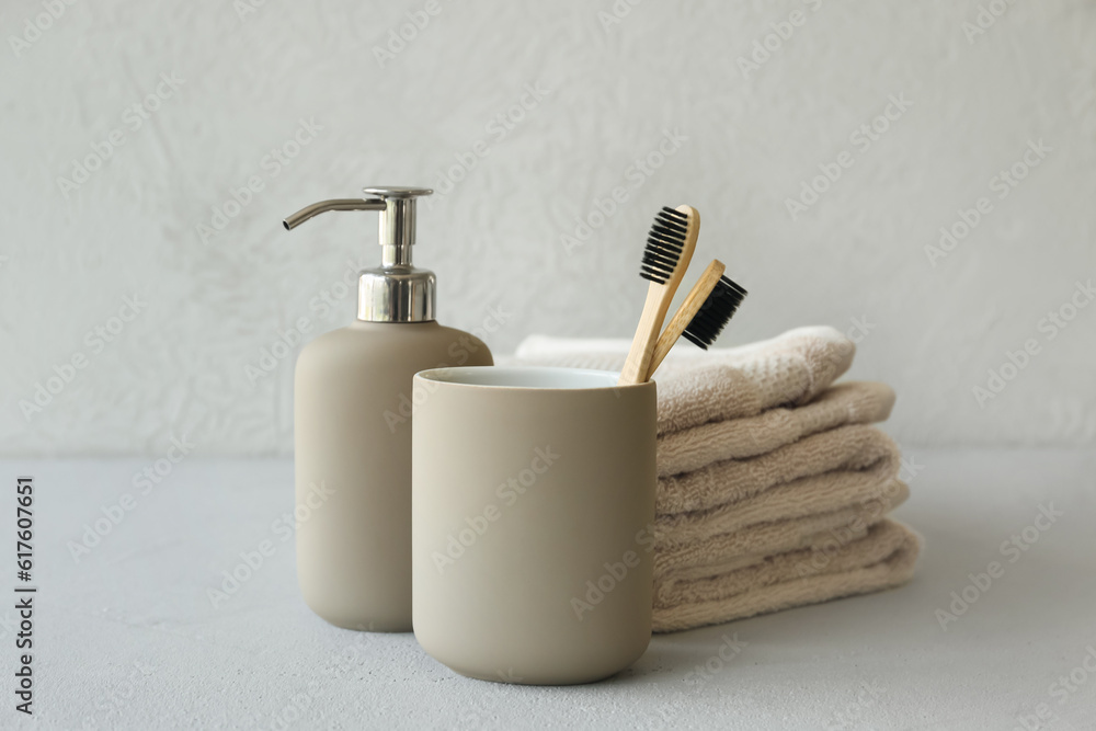 Bamboo tooth brushes in holder, liquid soap and towels on grey background