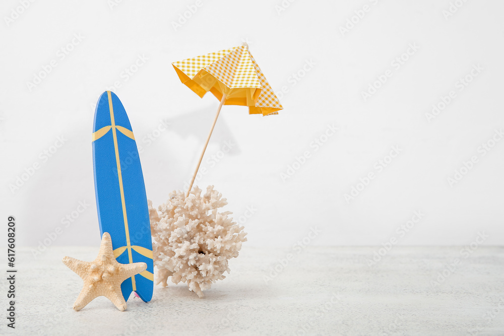 Mini surfboard with umbrella, coral and starfish on white table