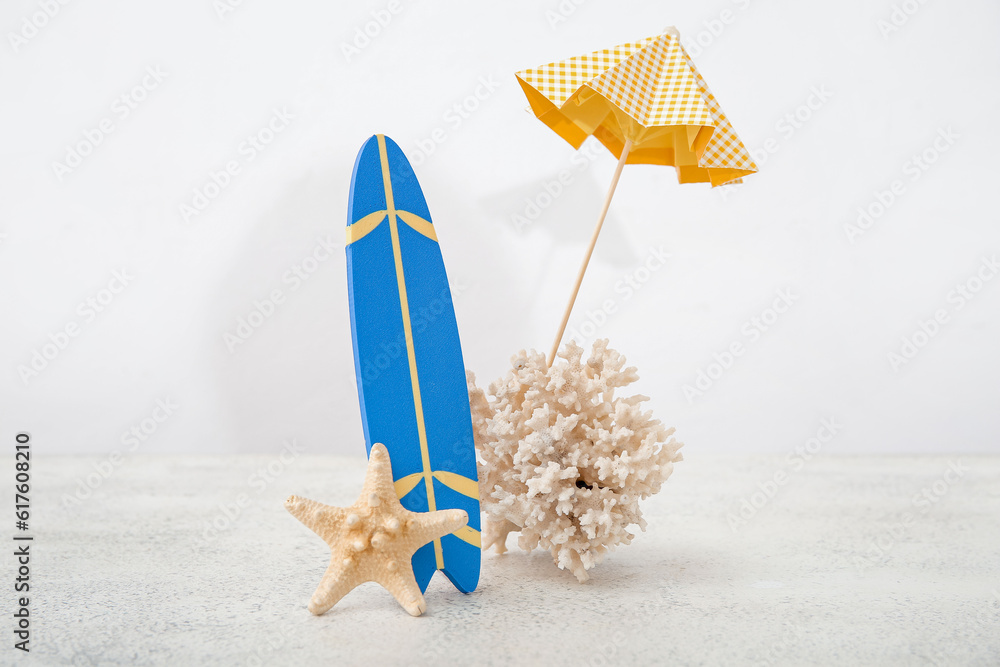 Mini surfboard with umbrella, coral and starfish on white table