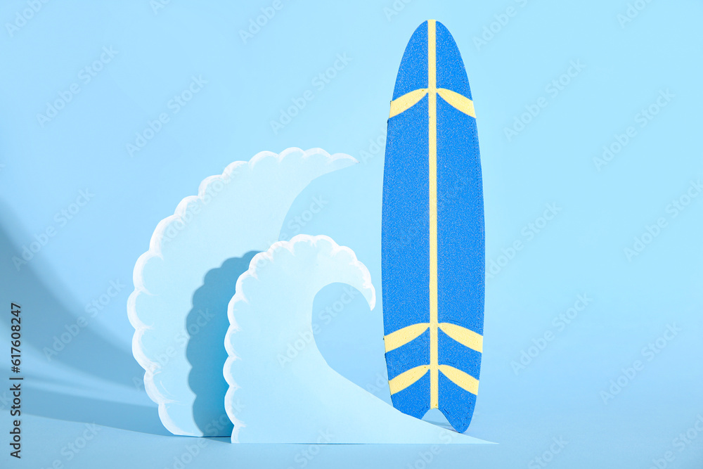 Creative composition with mini surfboard and paper waves on blue background