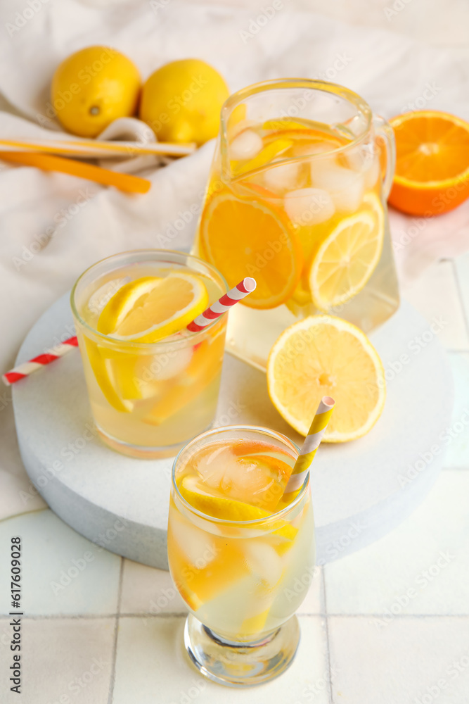 Glasses and jug of infused water with lemon on white tile background