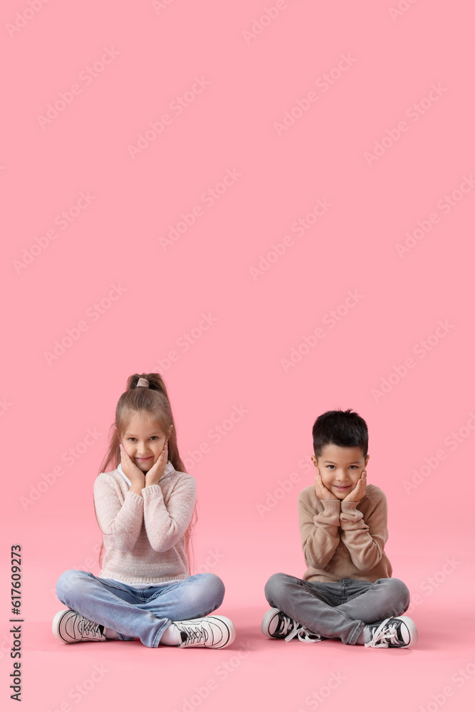 Cute little children in sweaters sitting on pink background