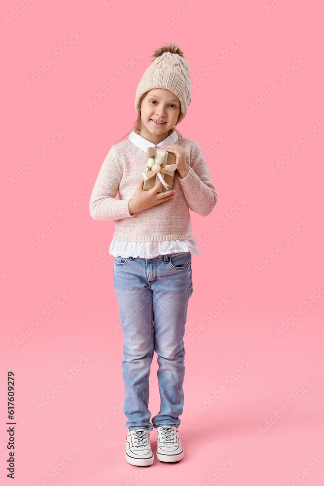 Cute little girl in sweater with gift on pink background