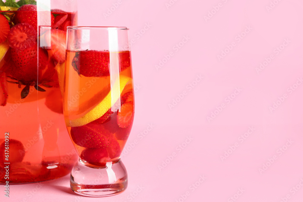 Glass and jug of infused water with strawberry on pink background