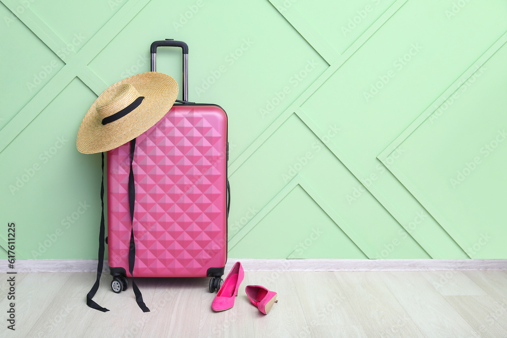 Suitcase with stylish wicker hat and high heels near green wall. Travel concept