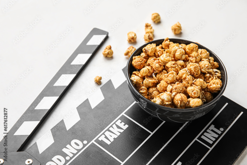 Bowl with tasty popcorn and clapperboard on white background