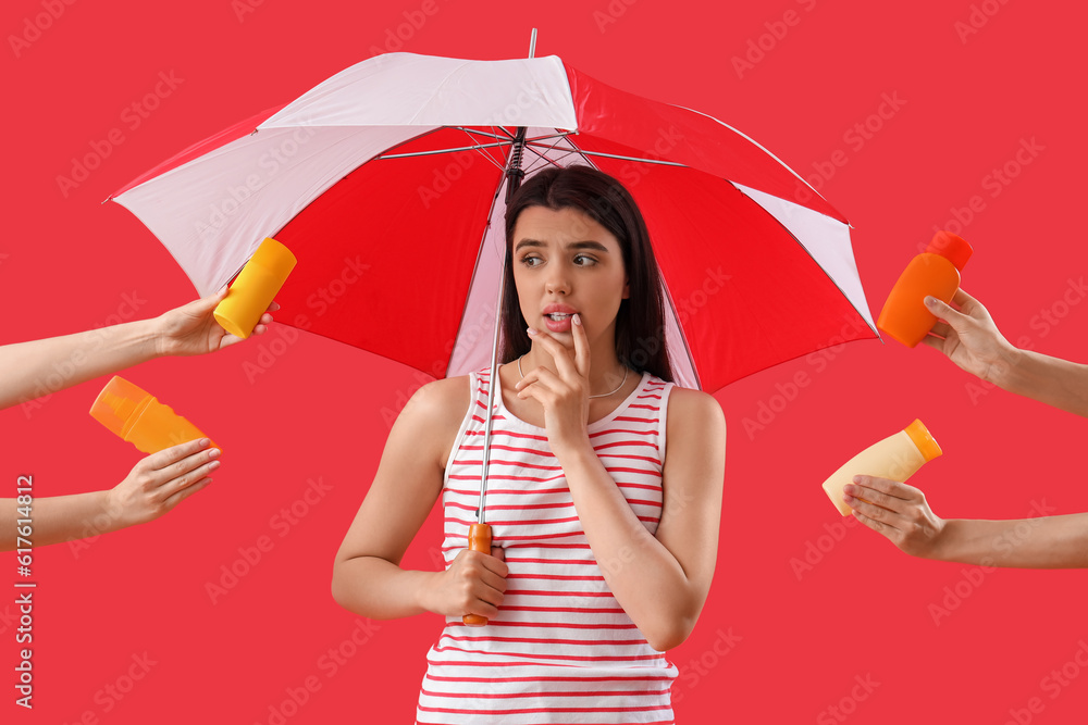 Thoughtful young woman holding beach umbrella and female hands with bottles of sunscreen cream on re