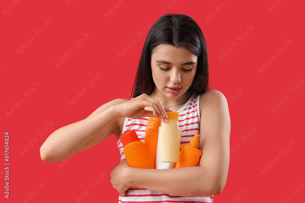 Young woman with bottles of sunscreen cream on red background