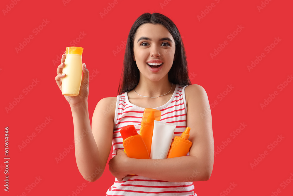 Young woman with bottles of sunscreen cream on red background