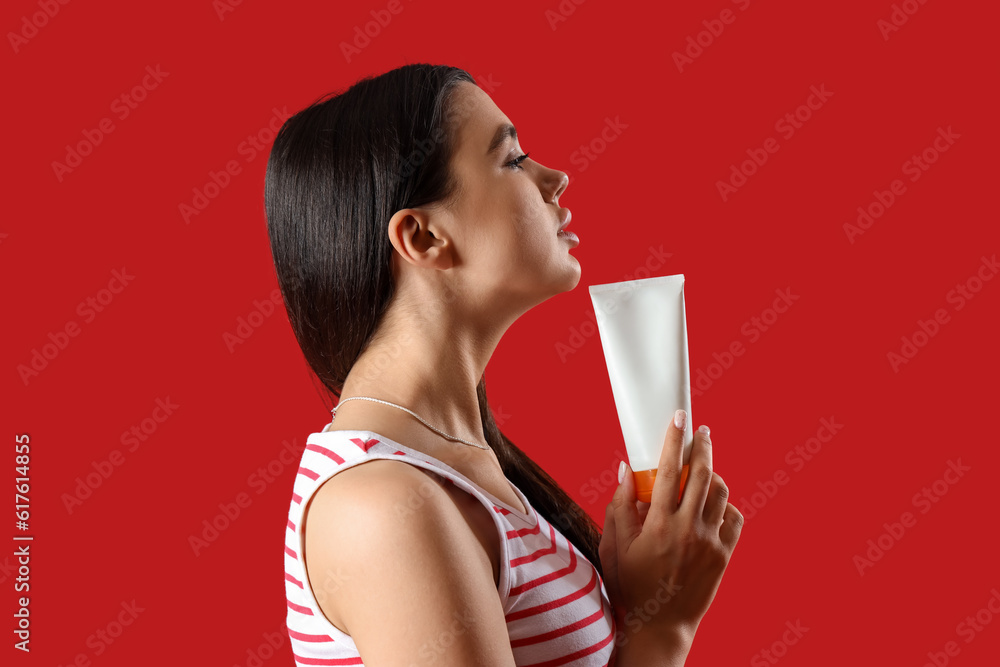 Young woman with sunscreen cream on red background, closeup