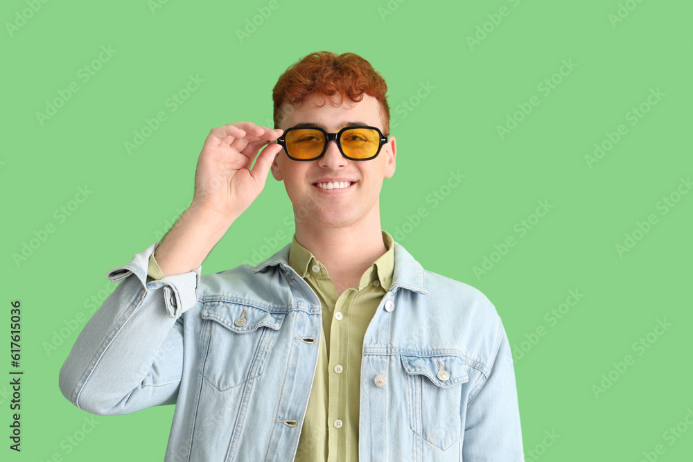 Young redhead man in sunglasses on green background