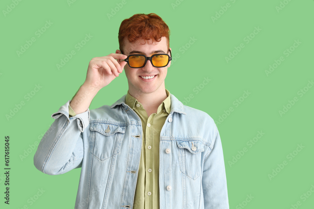 Young redhead man in sunglasses on green background