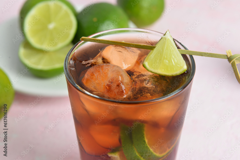 Glass of cold Cuba Libre cocktail on pink background