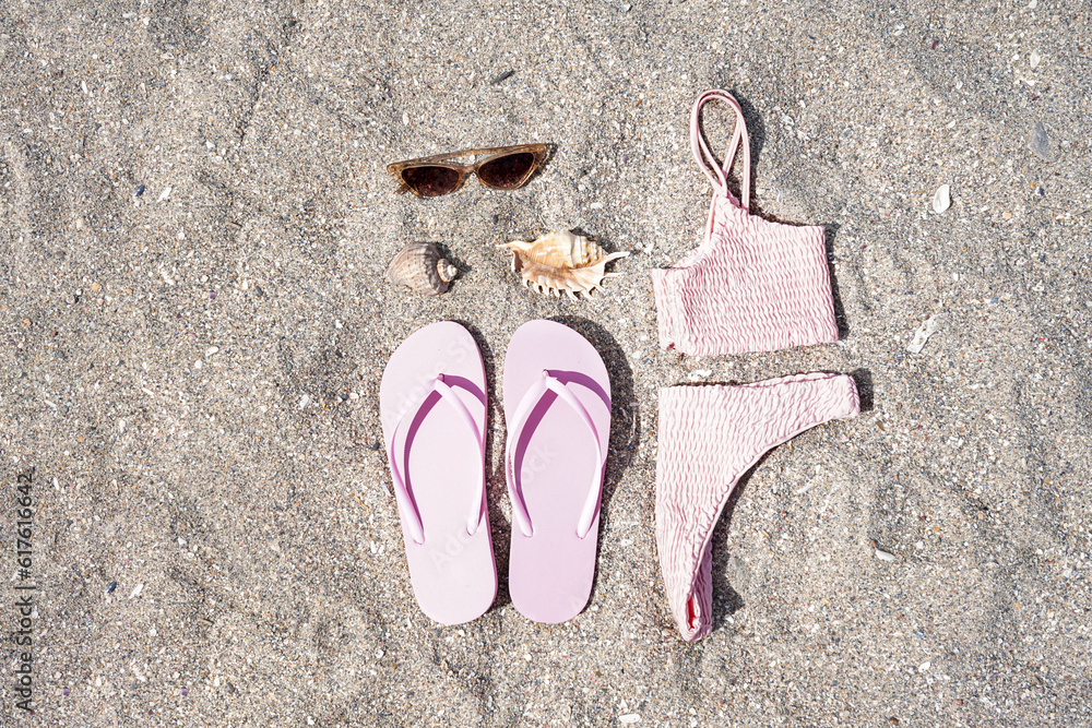 Pink flip-flops with swimsuit, sunglasses and shells on sand beach background