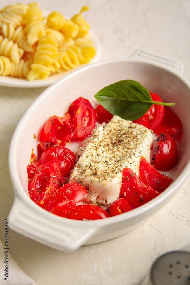 Baking dish with tasty tomatoes and feta cheese on light background