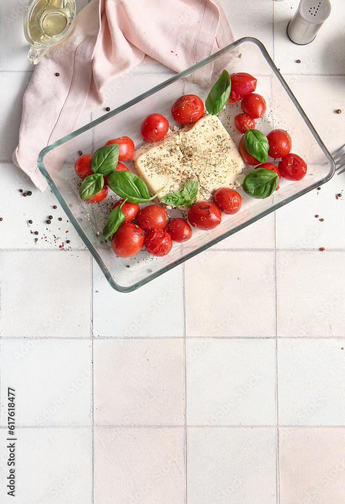 Baking dish with tasty tomatoes and feta cheese on white tile background