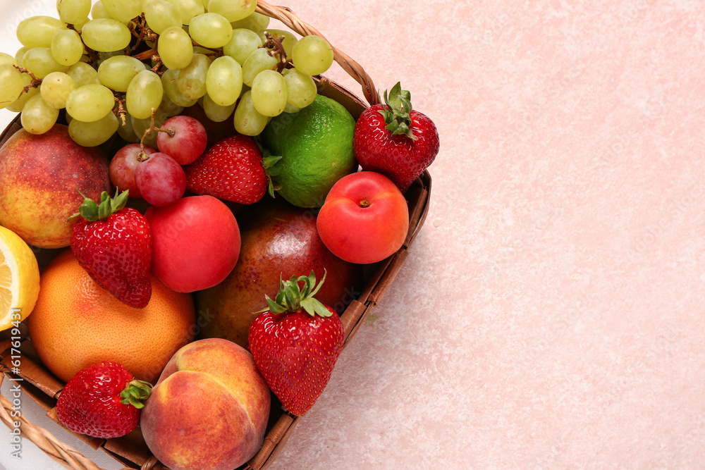 Wicker basket with different fresh fruits on pink background