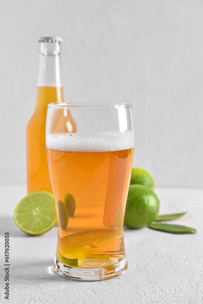 Glass of cold beer with lime on light background