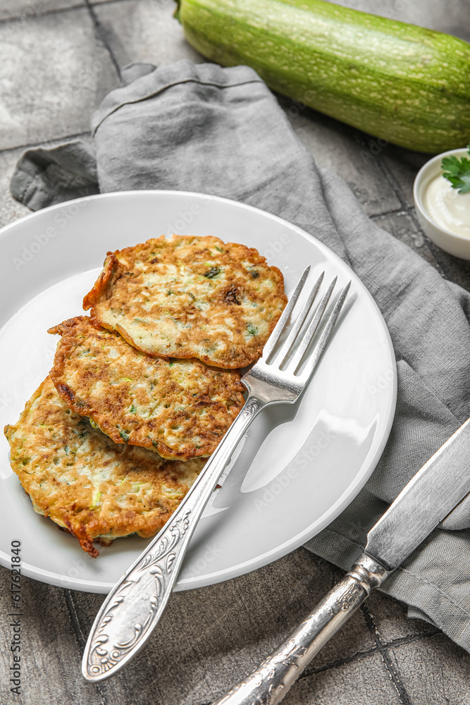 Plate of tasty zucchini fritters on grey tile background