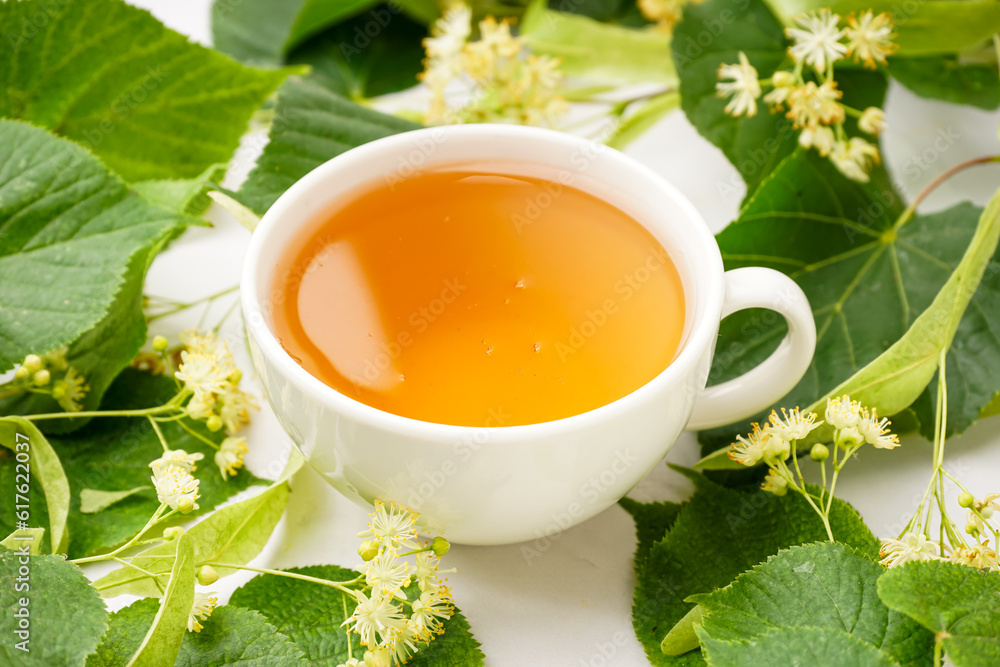 Cup of linden tea and leaves on white background