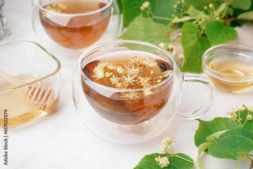 Glass cups of linden tea and bowls with honey on white background