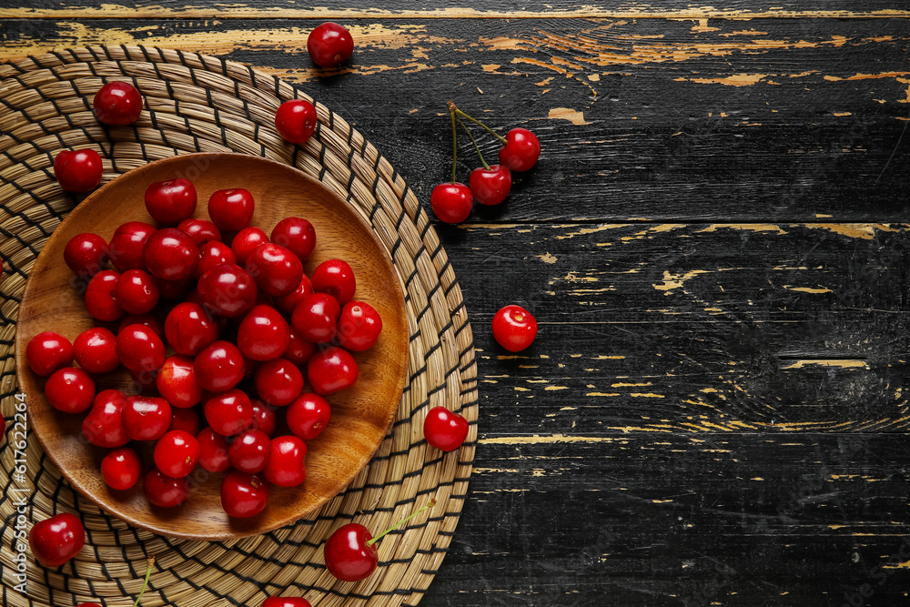 Plate with sweet cherries on black wooden background