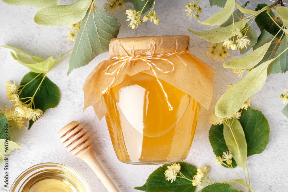 Glass jar of linden honey, dipper and fresh linden flowers on light background