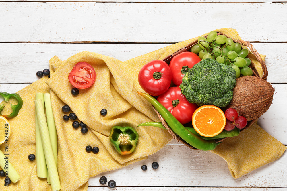 Wicker basket with different fresh fruits and vegetables on white wooden background