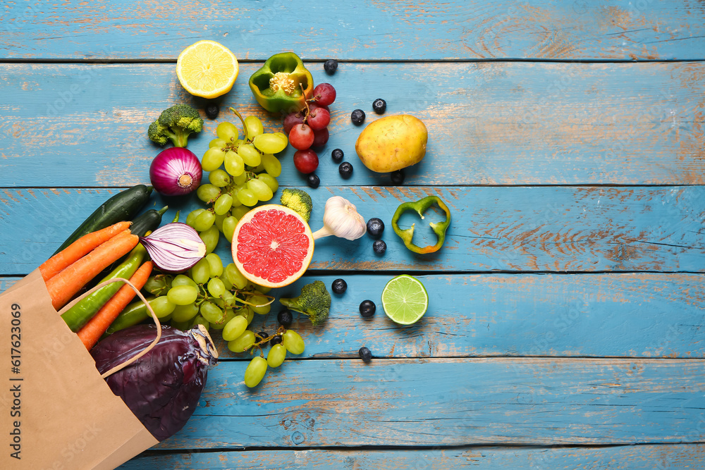 Paper bag with different fresh fruits and vegetables on blue wooden background