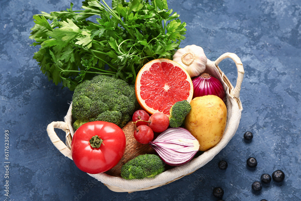 Wicker basket with different fresh fruits and vegetables on blue background