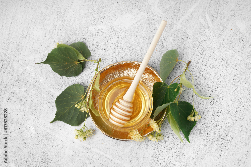 Plate with glass bowl of linden honey and dipper on grey background