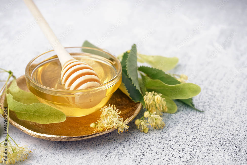 Plate with glass bowl of linden honey and dipper on grey background