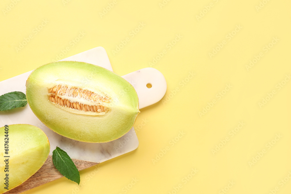 Board with pieces of sweet melon and mint on yellow background