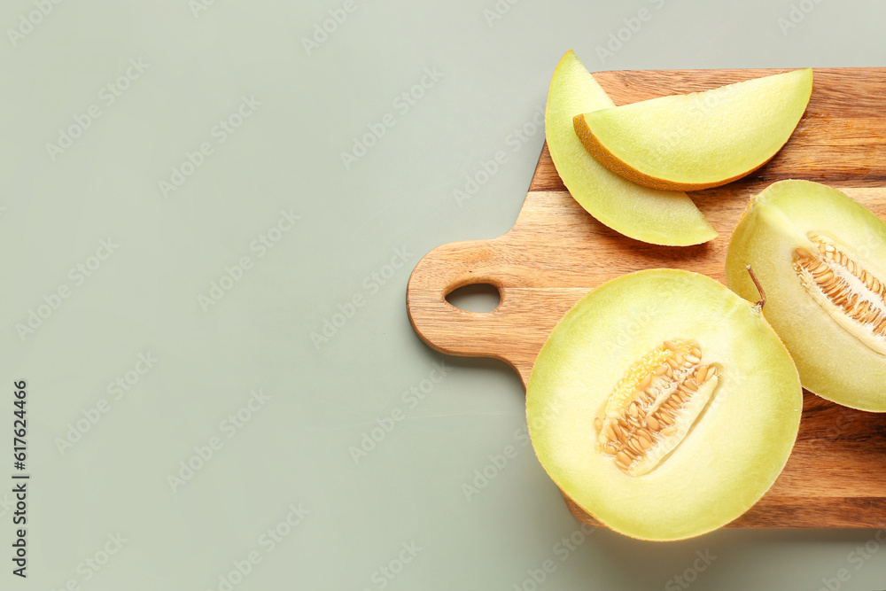 Wooden board with half of sweet melon and pieces on grey background