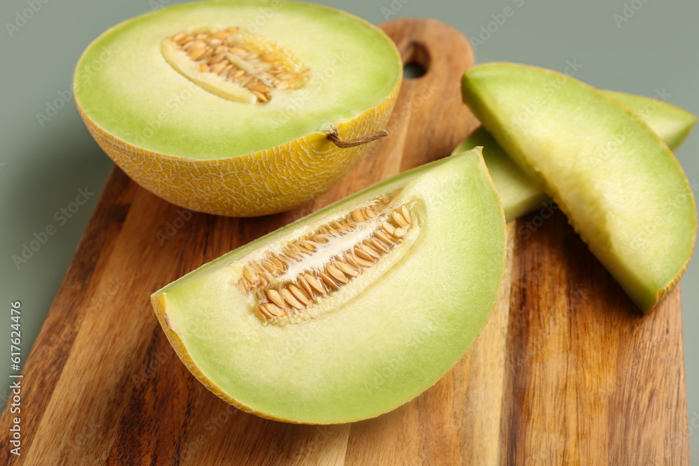 Wooden board with half of sweet melon and pieces on grey background