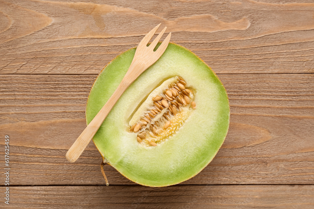 Half of sweet melon and fork on wooden background