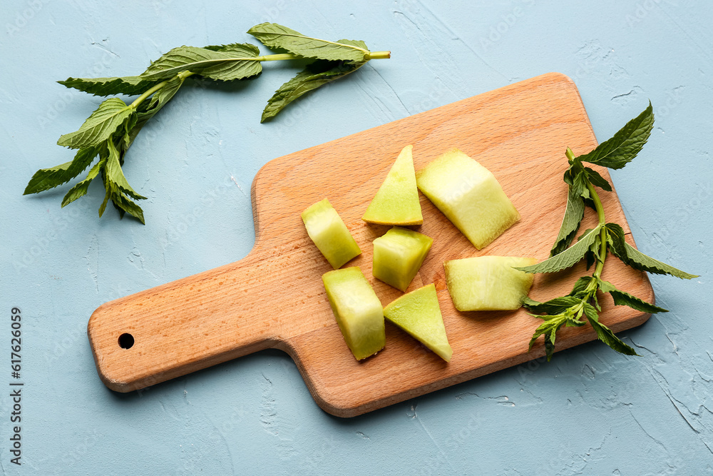 Wooden board with pieces of sweet melon and mint on blue background