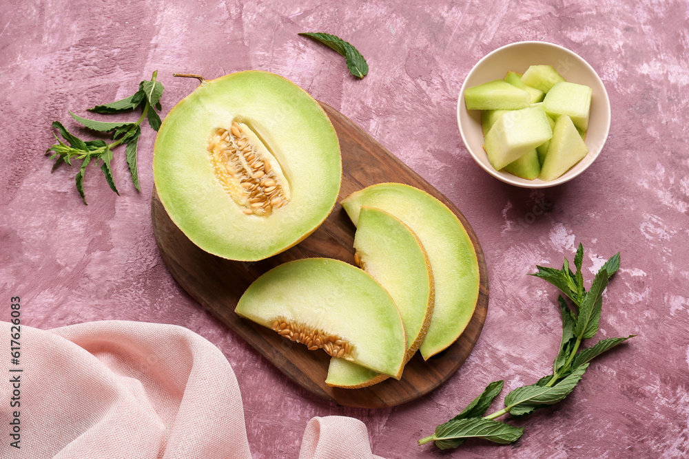 Wooden board with half of sweet melon and pieces on purple background