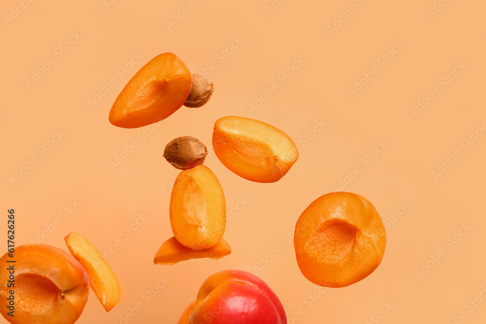 Flying halves of fresh apricot with pieces on orange background