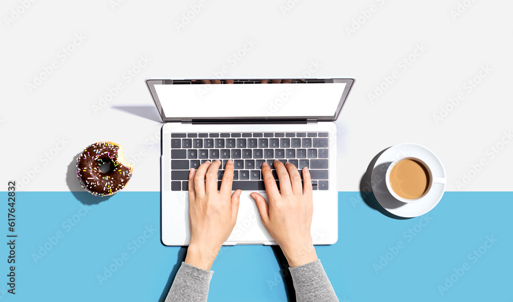 Person using a laptop computer with a donut and a cup of coffee - Flat lay