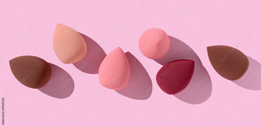 Multiple egg-shaped makeup sponges placed on a pink background.