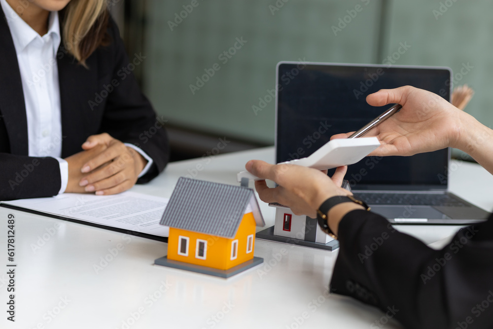 Businessman, real estate agent holding a calculator, presenting a price quote to a client for a hous