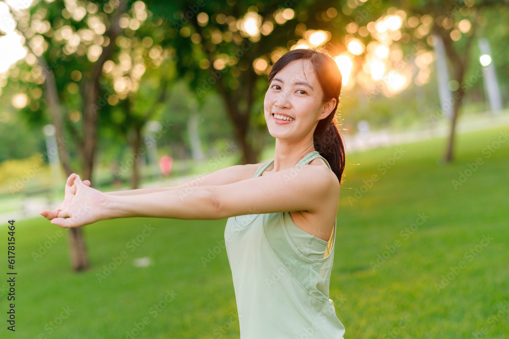 Female jogger. Fit young Asian woman with green sportswear stretching muscle in park before running 