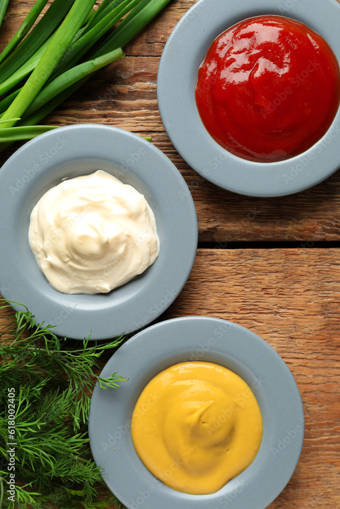 Plates with different sauces and herbs on wooden table