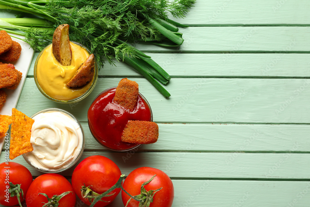 Composition with bowls of different sauces with vegetables and dipped snacks on green wooden table