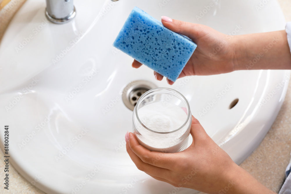 Woman cleaning white ceramic sink with baking soda, closeup