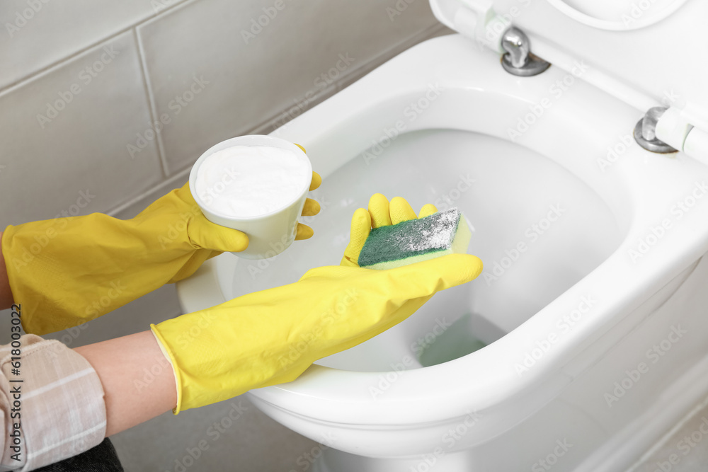 Woman in rubber gloves cleaning white toilet bowl with baking soda and sponge