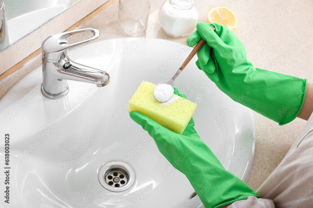 Woman in rubber gloves cleaning ceramic sink with sponge and baking soda, closeup