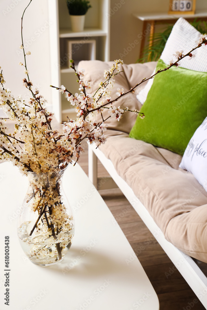 Vase with blooming tree branches on table in living room